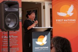 JoAnn standing and speaking into a mic behind a podium at the ribbon cutting ceremony. 